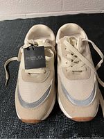 Front view of new Rachel Zoe women's sneakers, showing beige mesh and suede materials with reflective strip detail and lace-up closure. Brand tag attached.