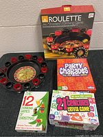 Photo showing all 4 items including the roulette drinking game with box, Party Charades game, 12 Drinking Games booklet, and 21st Century Trivia Game box.