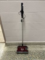 Full view of the Shark cordless stick vacuum cleaner standing upright against a wall on a terrazzo floor.