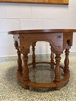Side view of the solid wood round side table showing turned legs and carved decorative supports.