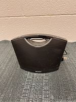 Front view of black Sony Bluetooth speaker showing mesh grille, carrying handle, and Sony logo.