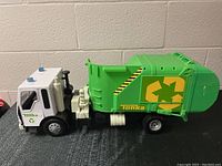 Side view of Tonka recycling truck toy showing white cab with blue lights and green rear loader with recycling symbol and caution striping.