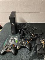Full view of Xbox 360 console, two wireless controllers, power cables, and game discs on a dark surface.