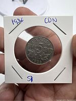 Reverse side of the Canadian 5 cents coin dated 1936, showing denomination, country name, year and maple leaf design, held in a cardboard coin holder with handwritten notes.