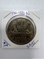 Obverse side of the 1966 Canada $1 silver dollar coin showing two men in a canoe with trees, date and inscriptions.