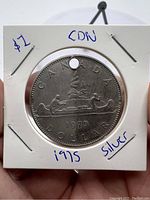 Obverse side of the 1975 Canadian silver dollar coin showing a canoe with two paddlers and the date 1975, with a hole punched at the top.