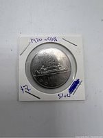 Photo of the reverse side of the 1980 Canadian silver dollar coin showing a voyageur paddling a canoe with the date and denomination.