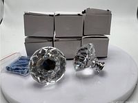8 clear faceted crystal glass knobs arranged with white boxes and screws in bag. Two knobs displayed outside boxes.
