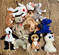 A top-down photo showing 11 Ty Beanie Babies plush toys laid out on a wooden surface. Includes a variety of animals and fantasy creatures identifiable by their distinct color, shape, and Ty heart-shaped tags on ears or sides.