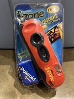 Front view of unopened Polaroid i-Zone camera in sealed packaging showing bright orange camera and Polaroid 6 photo film roll included.