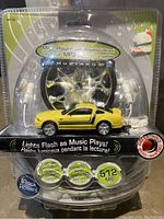 Front view of the sealed Mustang car shaped MP3 player with earphones and packaging showing key features like 512MB and music lights.