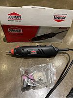 Photo of Jobmate rotary tool taken out of box with accessory bits in plastic bag and original cardboard box in background.
