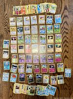 Overview of all Pokémon trading cards laid out on a wooden surface, showing multiple rows of cards and some stacked in piles.