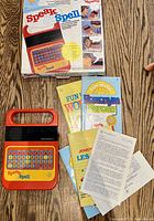 Speak & Spell toy along with original box and multiple manuals shown on a wood grain surface.