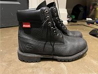 Side view of the black Timberland boots showing textured Helcor upper, metal eyelets, padded collar, and red Helcor tag.