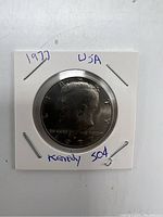 Front obverse side of 1977 Kennedy Half Dollar showing Kennedy's profile and date, sealed in white holder.