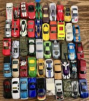 Photo showing a collection of 50 colorful vintage die cast toy cars arranged in rows, including sports cars, military tanks, and race cars.