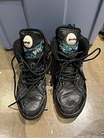Front view of pair Reebok Pump Blacktop Battleground shoes displaying black leather and patterned teal fabric uppers, laces tied but loose, creasing visible on toe box.