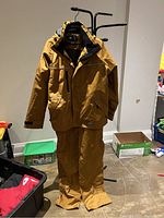 Photos of the brown men's winter dry suit jacket and pants displayed on a stand from front and back showing color, features, and condition.