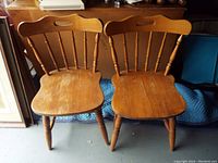 Pair of wooden spindle back chairs with visible wear and scratches on seats, showing traditional turned legs and handle cutout on the top rail of the backrest.