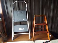 Photo showing both step ladders side by side, metal ladder with gray steps and wooden ladder worn finish
