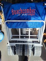 Folded Blue Beachcomber Mac Wagon beach cart showing the branded fabric bag and white metal frame with large rear tires