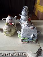 Full view of the lot showing all four ceramic teapots on a beige surface
