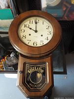 Front view of wooden regulator wall clock with round white dial and glass door with 'REGULATOR' label