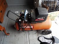Full view of orange Craftsman air compressor with black motor housing and wheels.