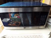 Front view of GE stainless steel microwave oven with black glass door and control panel on right side, showing overall item condition.