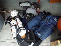Photo showing Bauer helmet, Easton gloves, Bauer knee/shin guards, elbow pads, hockey pants and shoulder pads arranged on floor.
