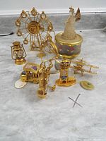 Photo showing entire lot of 8 gold plated figurines including Ferris wheel, carousel, lantern, helicopter, golf cart, vintage car, crystal angel, and music box base.