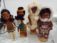 Four Native American dolls displayed standing on a surface, showcasing traditional clothing and head accessories.