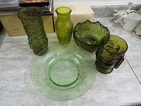 Overview of six green glassware items including vases, bowl, plate, and mug arranged on a surface.
