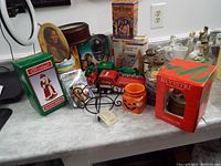 Overview of lots showing a variety of collectible and decorative items on a table including Silvestri snow globe, Budweiser Santa, and other figurines.