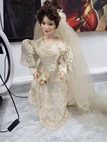 Full view of the porcelain bride doll standing on the floor with visible ivory lace wedding dress and veil detail.