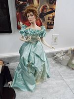 Full view of porcelain doll standing on floor against a wall, wearing light green dress and cream gloves, 23 inches tall.