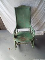 Front view of green wooden rocking chair showing full seat, backrest, and armrests with visible wear and paint chipping.
