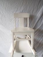 Front view of small white wooden rocking chair showing overall structure and rocker bases