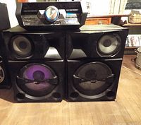 Front view of Sony HCD Shake stereo main unit placed on top of two large Sony speakers; left speaker lit with purple light effect, right speaker unlit