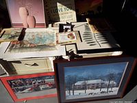 View of various wall signs, prints, sayings, and framed art on table with shadows, showing sizes and condition.