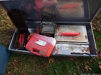 Aluminum chest with red plastic carrying case, extension cord and various tools stored inside showing condition of chest and contents