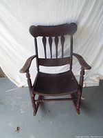 Front view of vintage wooden rocking chair showing seat, armrests, and spindled backrest with purple paint and signs of wear.