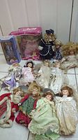 Lot of 13 collectible dolls shown on floor, including boxed Disney doll and various unboxed porcelain dolls in vintage style clothing.