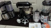 KitchenAid Artisan mixer alongside Ninja coffee maker and Cuisinart blender with attachments and accessories displayed.