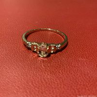 Front view of 10K rose gold ring displaying the semi-precious center stone, side stones, and small diamonds on setting edges against a red background.