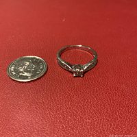 Photo of 10K white gold diamond ring next to a quarter for scale on a red surface, showing overall condition and size.