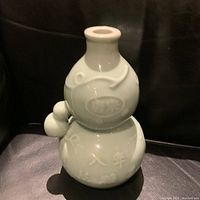 Front and side view of double gourd celadon vase showing embossed Asian characters and decorative motifs.