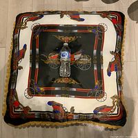 Top view of extra-large square pillow with a water bottle placed at center for size reference; pillow has a horse carriage print on black and cream fabric with gold lace edge.