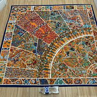 Full view of square silk scarf laid flat on wood floor with water bottle for scale